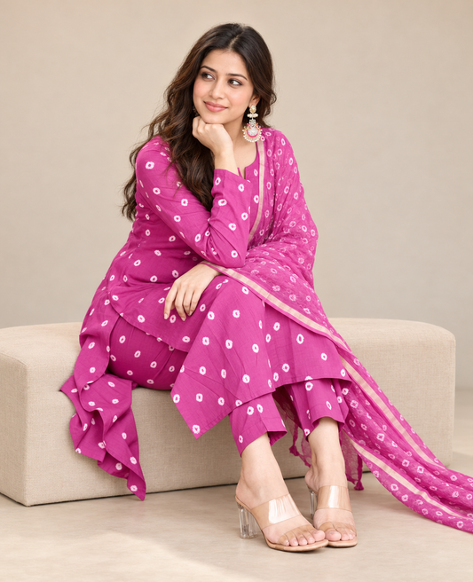 Model wearing a magenta Bandhani print Anarkali kurta with white motifs, matching pants and a sheer bordered dupatta against a beige background.
