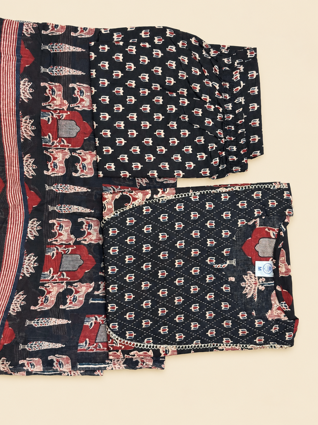 A folded dark navy or black fabric garment with a repeating small floral block print in red, pink, and white, plus a striped border and matching printed textile piece, laid flat on a light beige background.