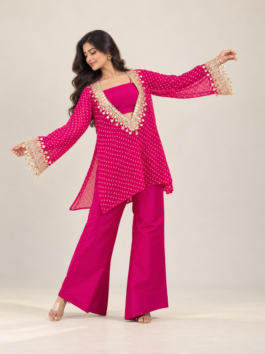 A woman modeling a bright fuchsia pink traditional outfit with a matching kurta and wide-leg pants, decorated with gold embroidery and beadwork, set against a plain light beige studio background.