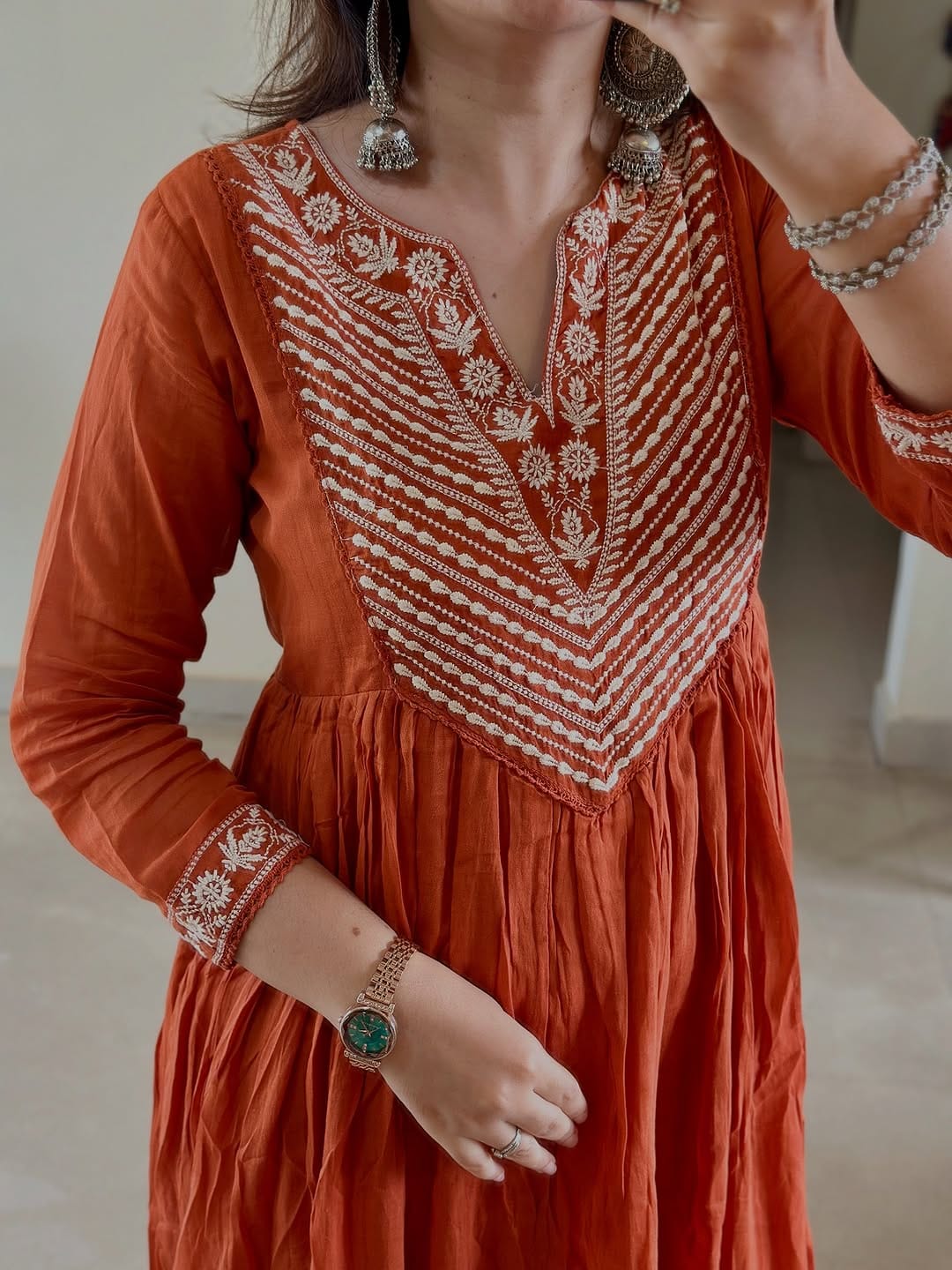 Person wearing an orange dress with intricate white embroidery, holding a phone.