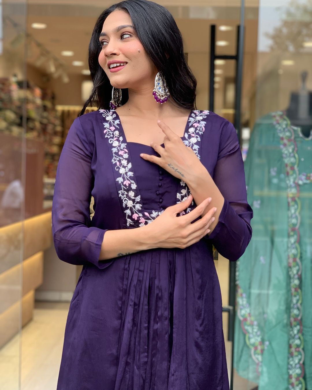 Woman wearing a purple dress with floral embroidery in a store setting