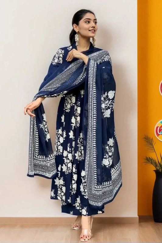 A woman models a navy blue traditional outfit with white floral prints and border embroidery, featuring a long kurta, wide sleeves, and a matching dupatta, set against a split beige and orange background.