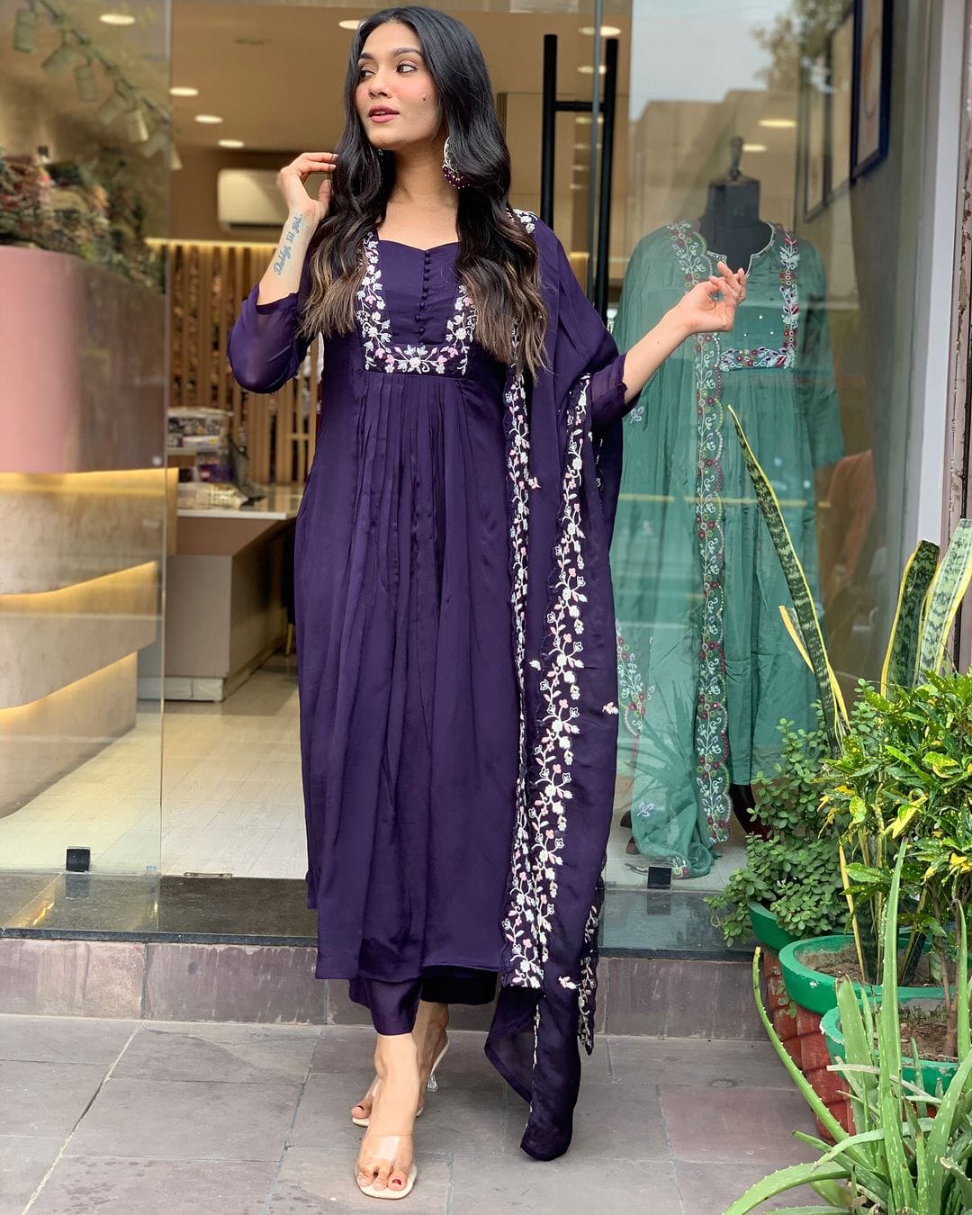 Woman in a purple traditional outfit standing in front of a store entrance.